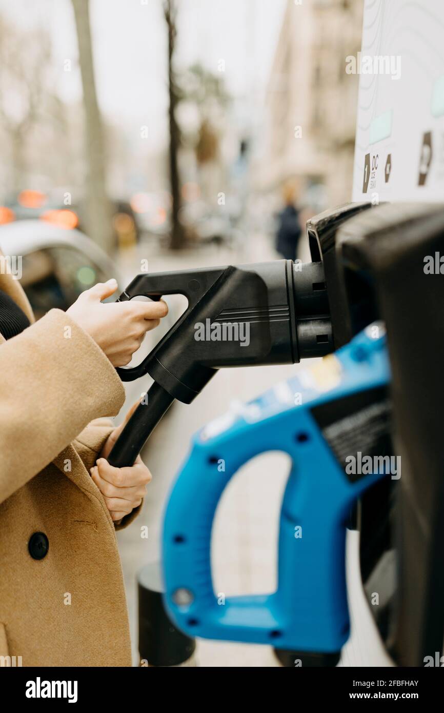 Femme tenant le cordon de la voiture électrique à la station de charge Banque D'Images