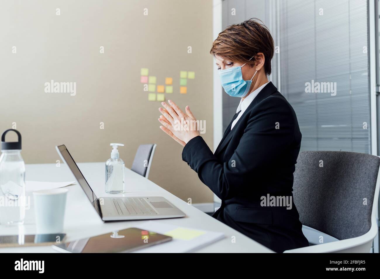 Femme professionnelle avec masque facial de protection frottant les mains pendant l'utilisation assainisseur au bureau dans le bureau Banque D'Images