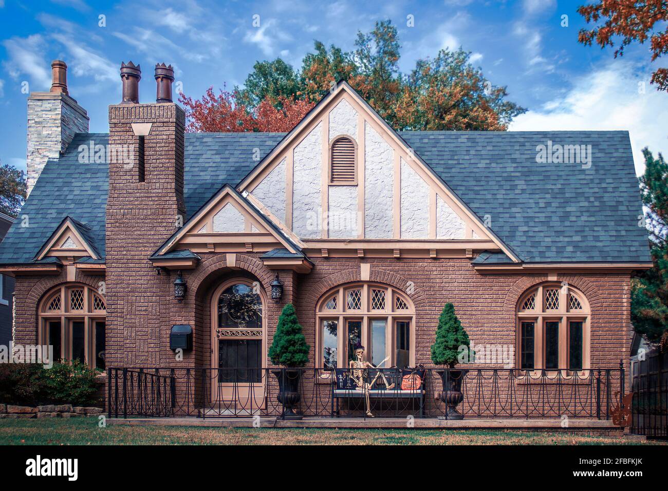 Charmant cottage en brique d'époque avec couleurs d'automne et Halloween squelette sur un banc extérieur porte avant - fenêtres cintrées et porte Banque D'Images