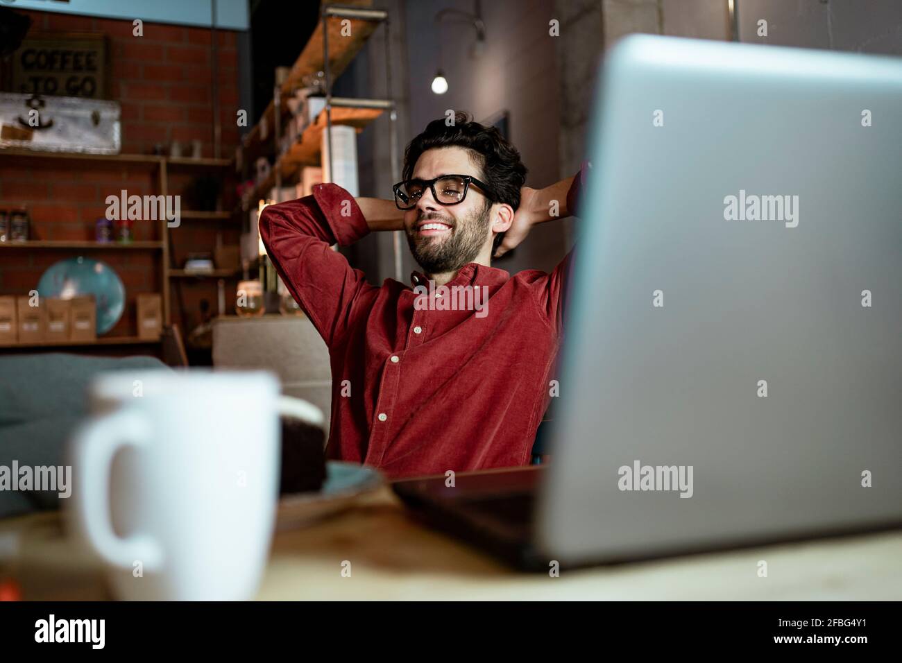 Travailleur indépendant souriant avec les mains derrière la tête dans le café Banque D'Images