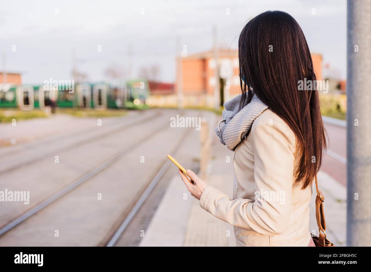 Femme aux cheveux longs tenant un smartphone en attendant train à la plate-forme de chemin de fer Banque D'Images