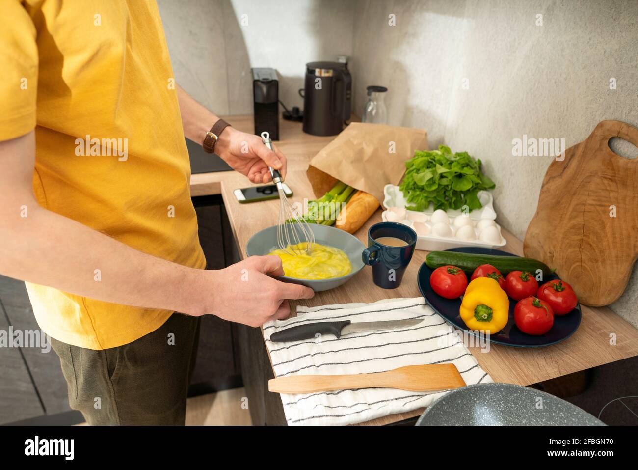 Homme stiring oeufs dans un bol avec le batteur sur le comptoir de cuisine à la maison Banque D'Images