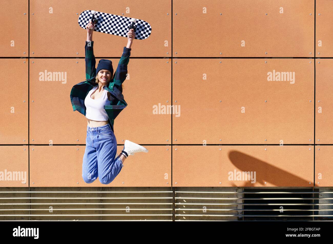 Femme insouciante avec le transport de planche à roulettes tout en sautant devant le mur Banque D'Images Femme insouciante avec le transport de planche à roulettes tout en sautant devant le mur Banque D'Images