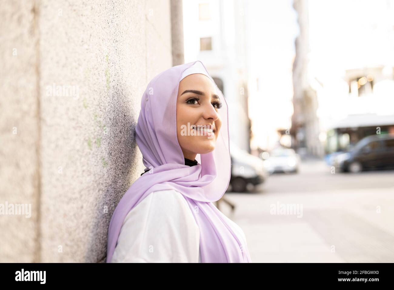 Belle adolescente dans hijab regardant loin tout en se tenant mur en ville Banque D'Images