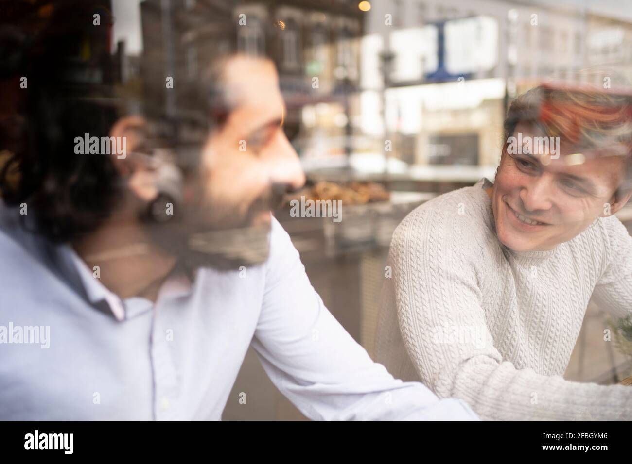 Des collègues de sexe masculin discutant dans un bureau de collègue pendant une pause-café vu à travers le verre Banque D'Images