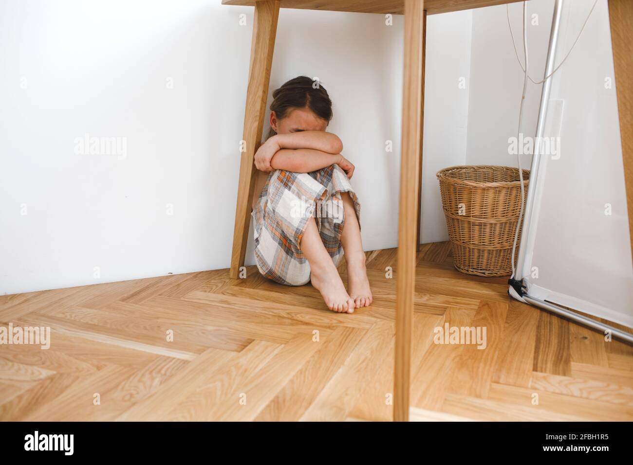 Petite fille enfoncée assise sous une table au sol à la maison Banque D'Images