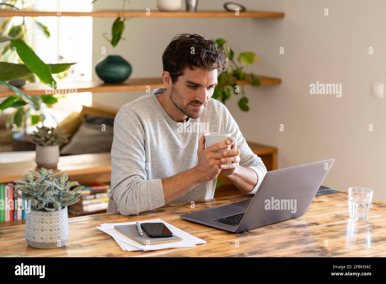 Travailleur indépendant concentré ayant du café tout en regardant l'ordinateur portable dans bureau à domicile Banque D'Images