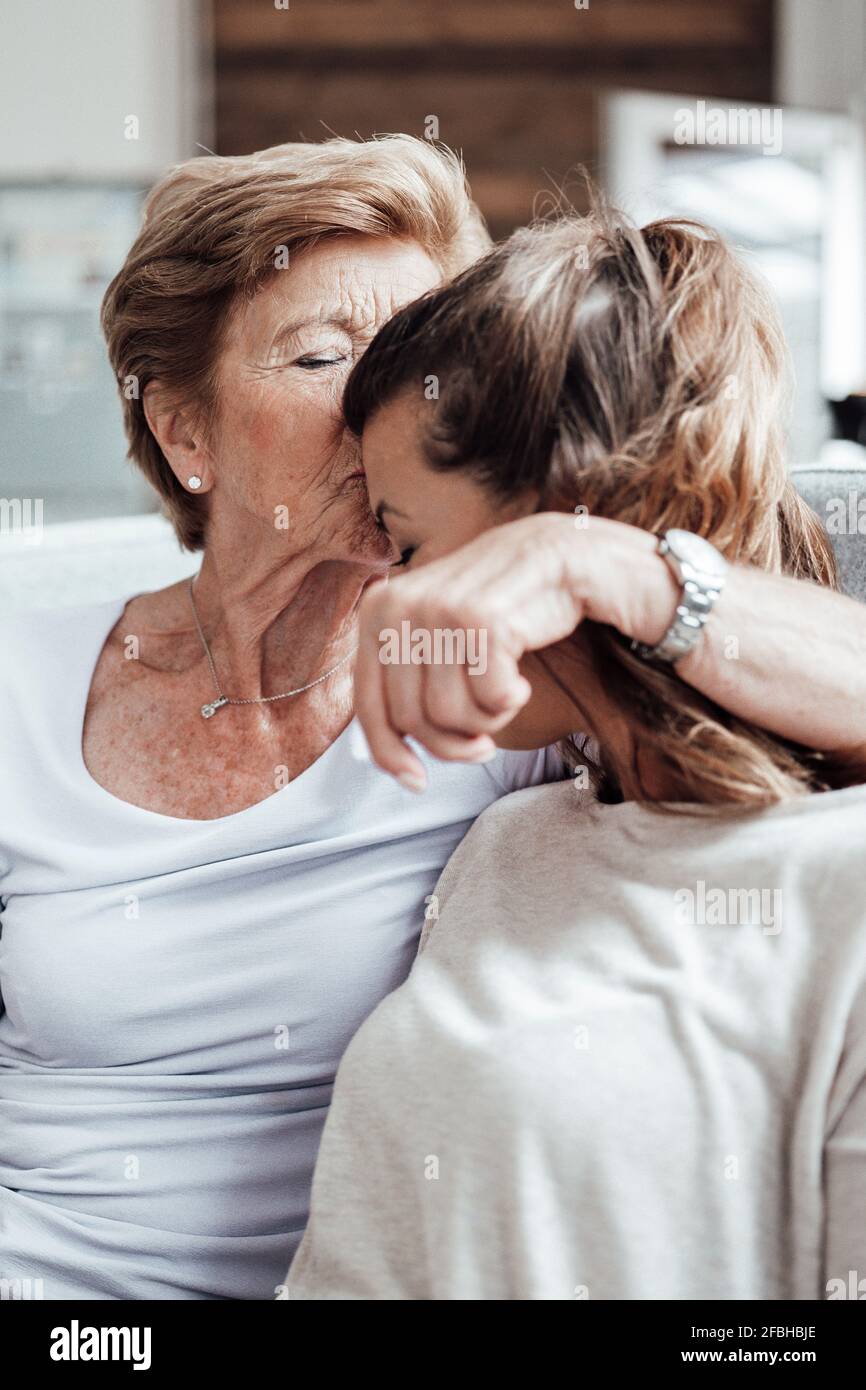 Grand-mère attentionnée embrassant la petite-fille sur le front tout en étant assise à la maison Banque D'Images