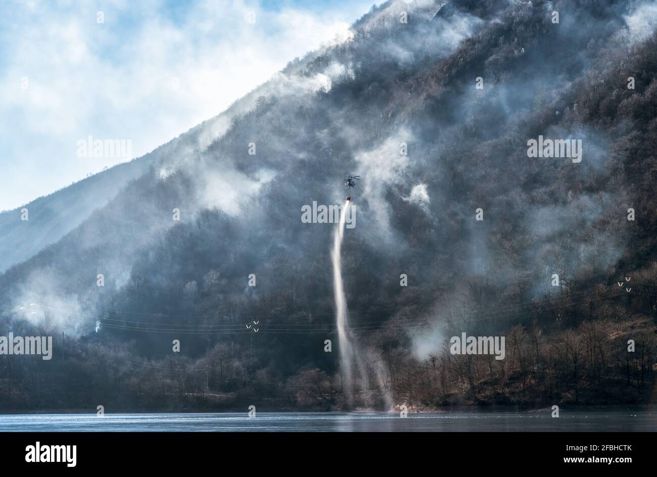 Incendie de la montagne Mondonico au-dessus du lac Ghirla avec un hélicoptère qui charge de l'eau pour l'extinction, Valganna, Lombardie, Italie. Banque D'Images