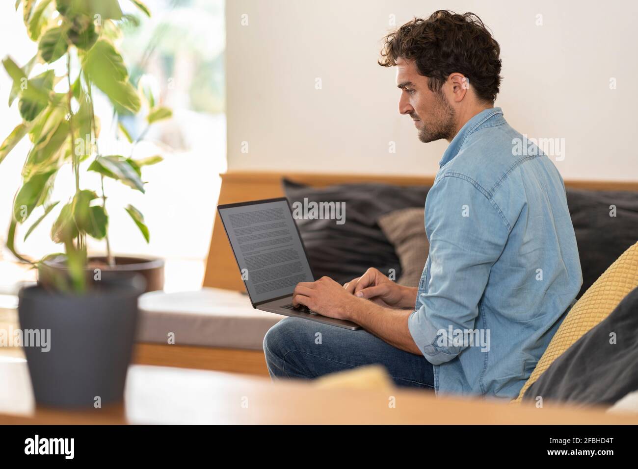 Travailleur indépendant masculin concentré assis sur un canapé avec un ordinateur portable à accueil Banque D'Images
