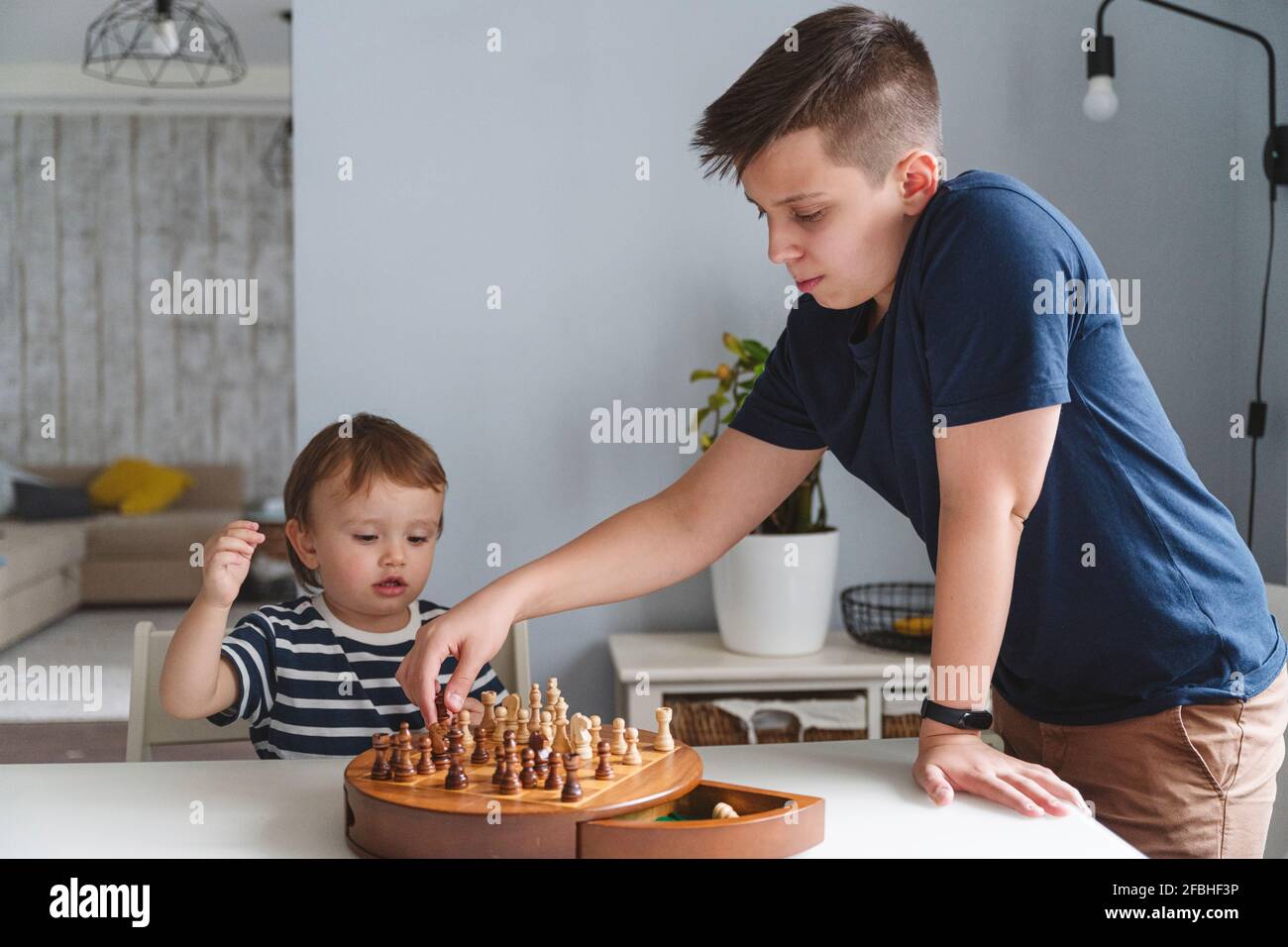 Frères et sœurs jouant au jeu d'échecs sur une table dans un appartement moderne Banque D'Images