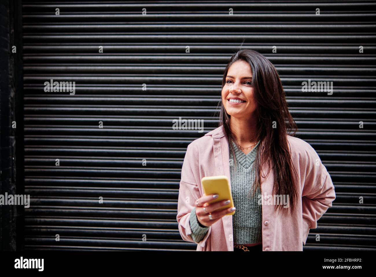 Femme souriante regardant loin en se tenant devant la fermé obturateur Banque D'Images