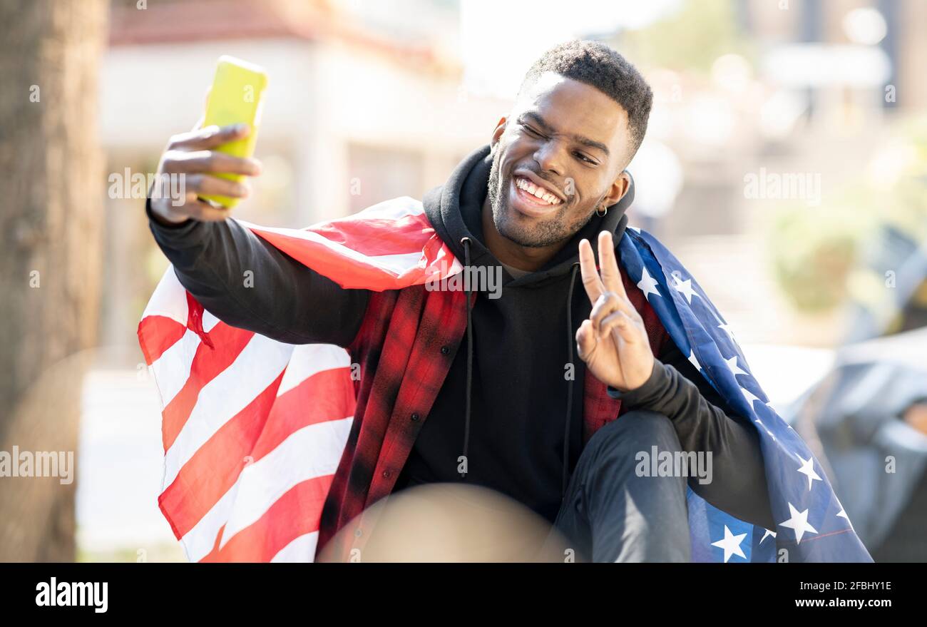 Un jeune homme qui prend le selfie avec le drapeau américain tout en montrant la paix signe et clin d'œil Banque D'Images