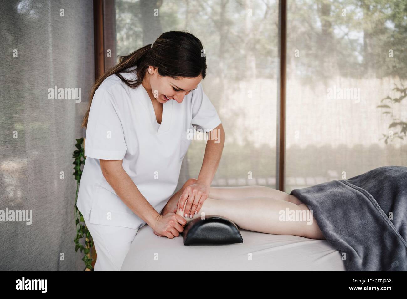 Femme souriante physiothérapeute massant le pied du patient en clinique Banque D'Images