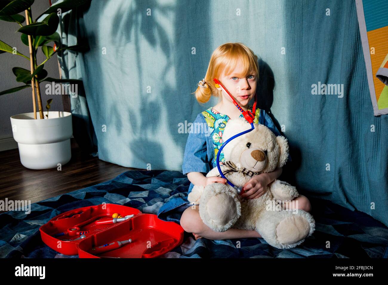 Fille blonde aspirante jouant avec stéthoscope et ours en peluche à accueil Banque D'Images