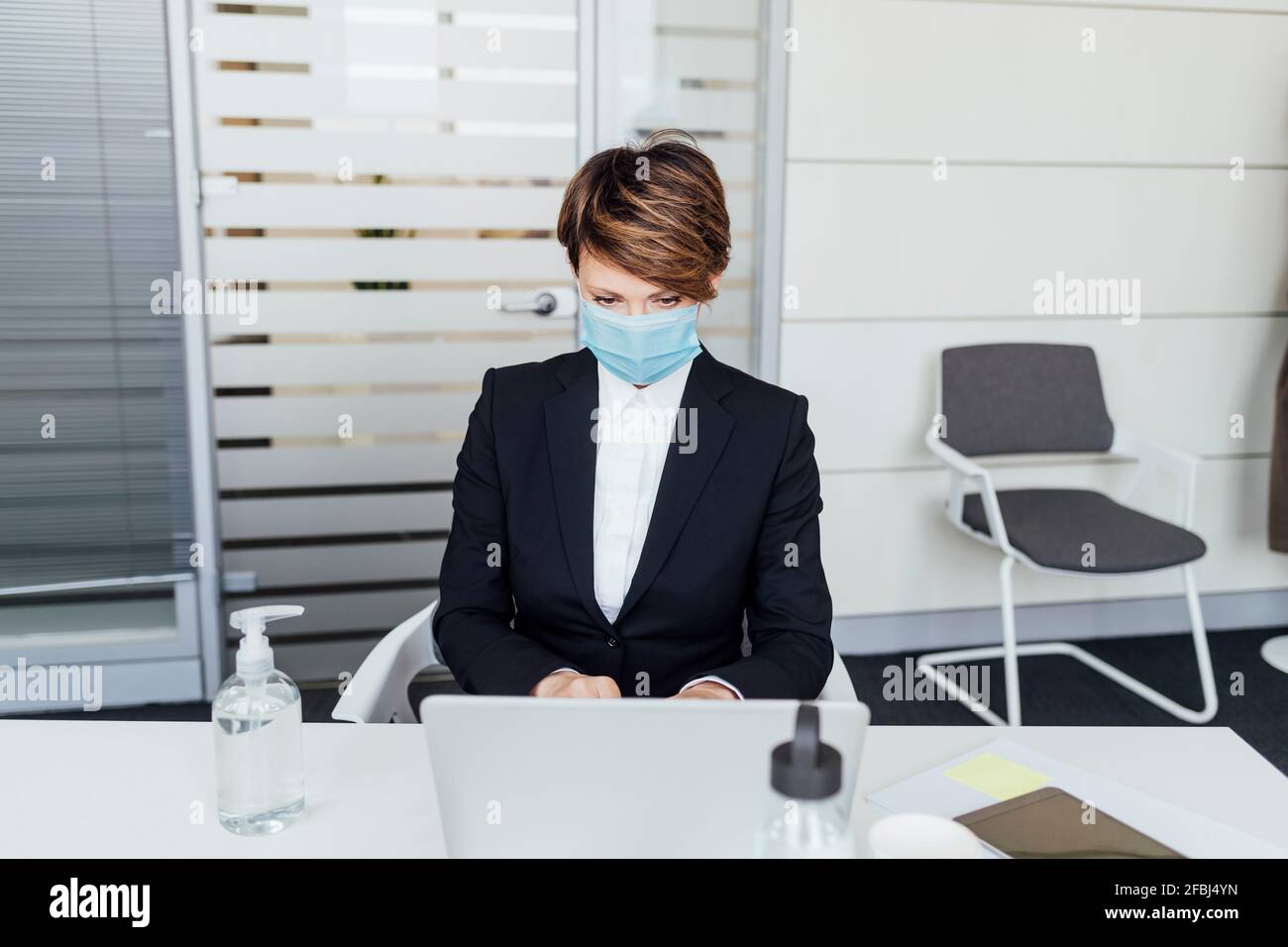 Femme d'affaires avec masque de protection travaillant sur un ordinateur portable au bureau Banque D'Images