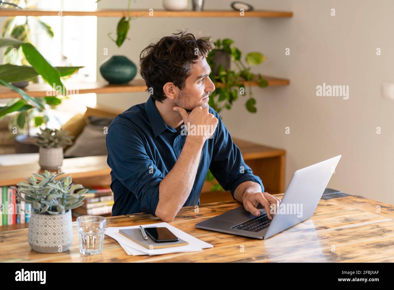 Travailleur indépendant de sexe masculin qui envisage d'utiliser un ordinateur portable à table Banque D'Images