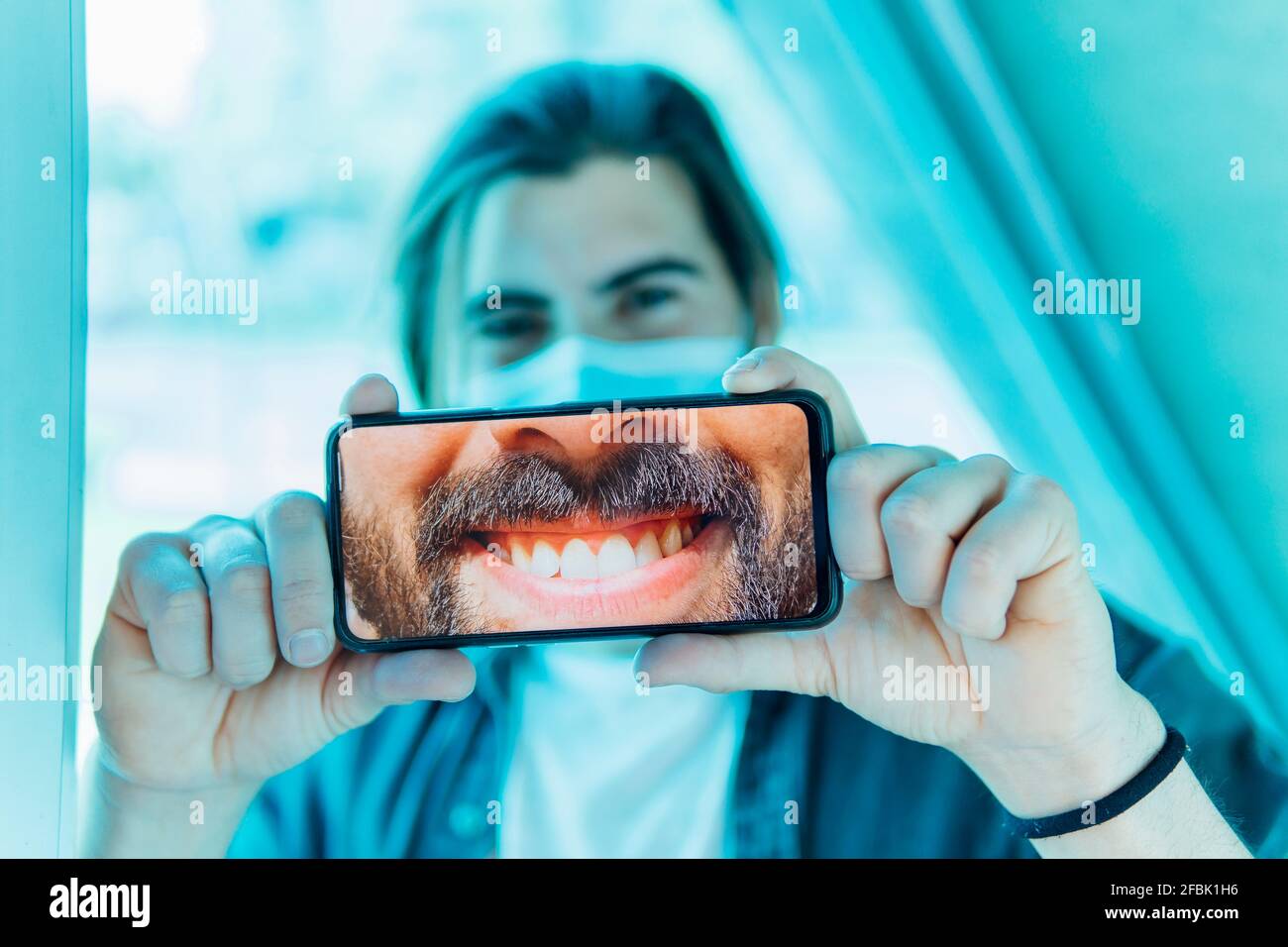 Jeune homme montrant un sourire crasseux sur un téléphone portable pendant le Covid-19 Banque D'Images