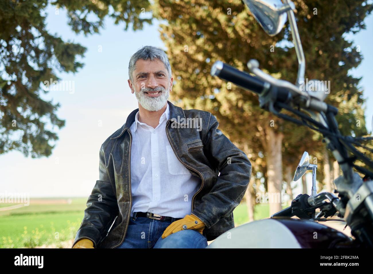 Homme souriant portant une veste de moto assise sur une moto Banque D'Images