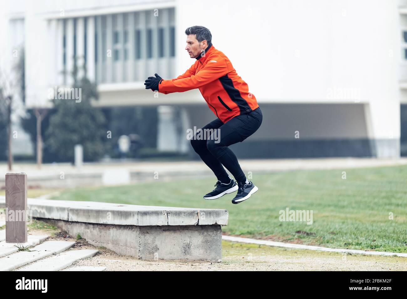 Homme sportif qui fait sauter des squats sur le mur de soutènement en