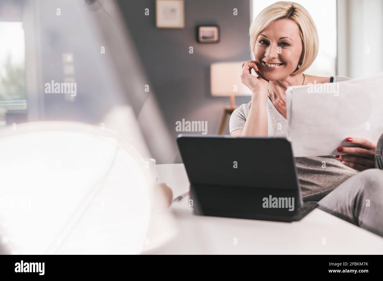 Femme souriante avec une tablette numérique et du papier à la maison Banque D'Images