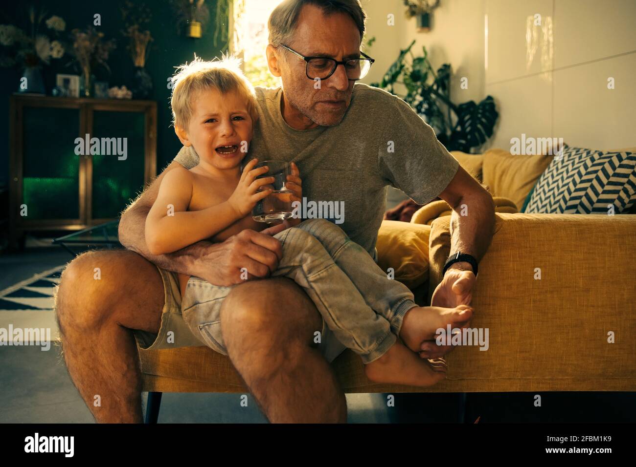 Père regardant pleurer le pied de son fils tout en étant assis sur le canapé à la maison Banque D'Images