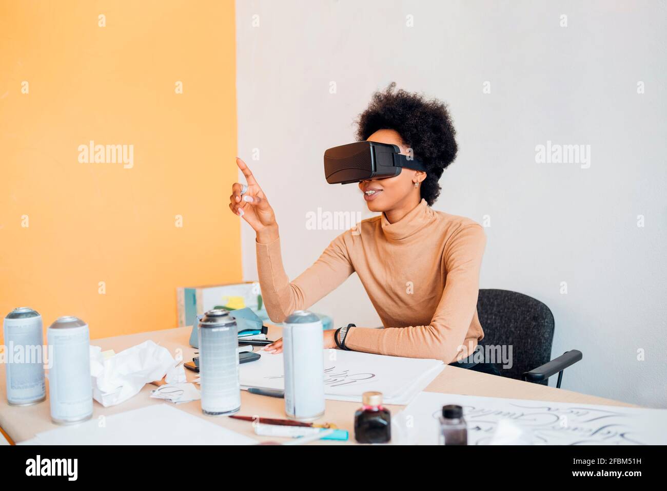 Jeune Afro femme portant le simulateur de réalité virtuelle gestante pendant qu'elle est assise à la table en studio Banque D'Images