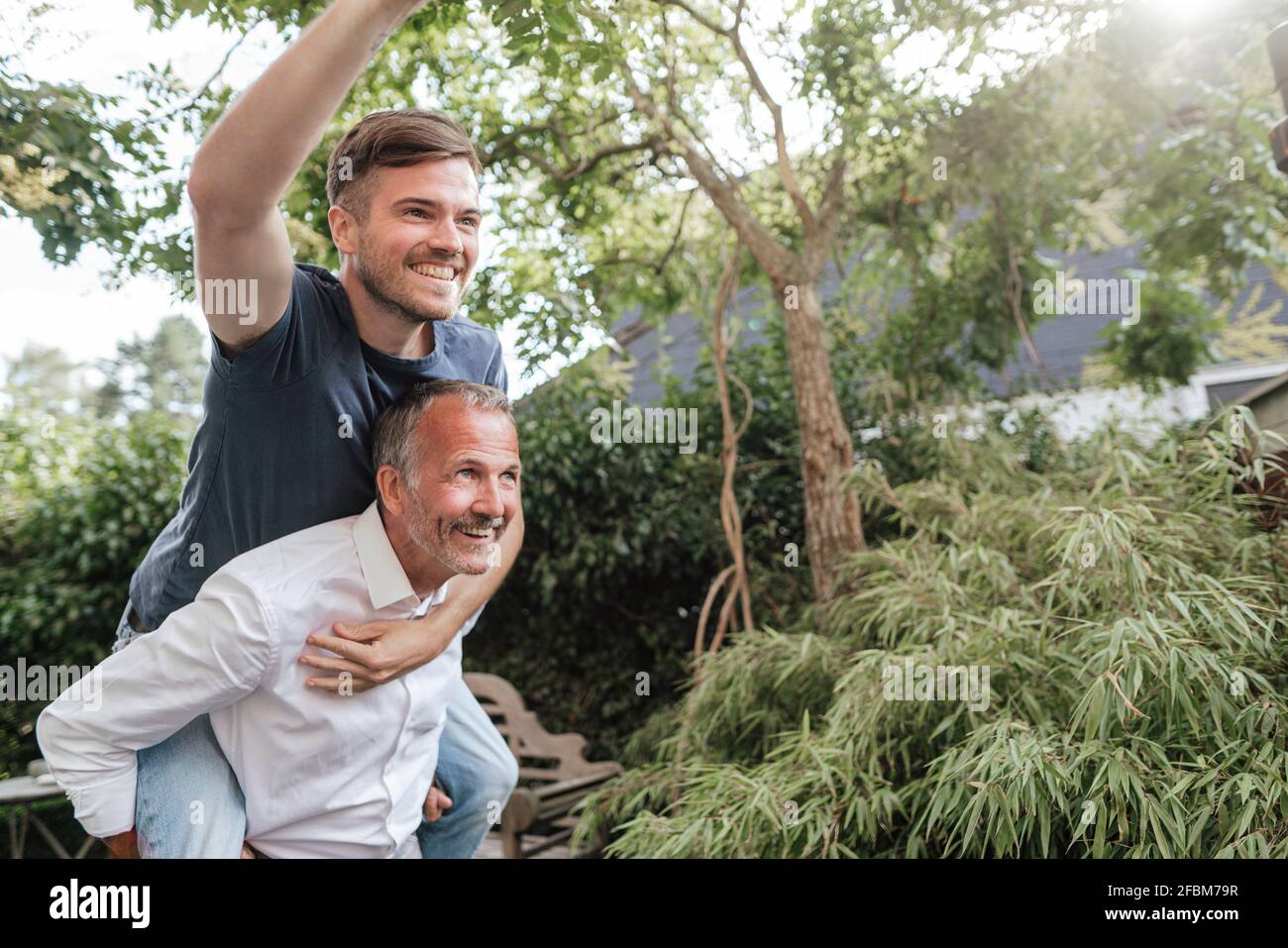 Père donnant une promenade en pigeyback à un fils joyeux dans l'arrière-cour Banque D'Images