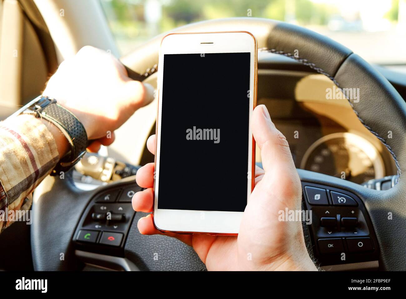 Jeune homme tenant un téléphone cellulaire à écran vide en conduisant. Un conducteur homme a la main sur le volant et a vérifié son smartphone dans un véhicule en mouvement. Ne le faites pas Banque D'Images