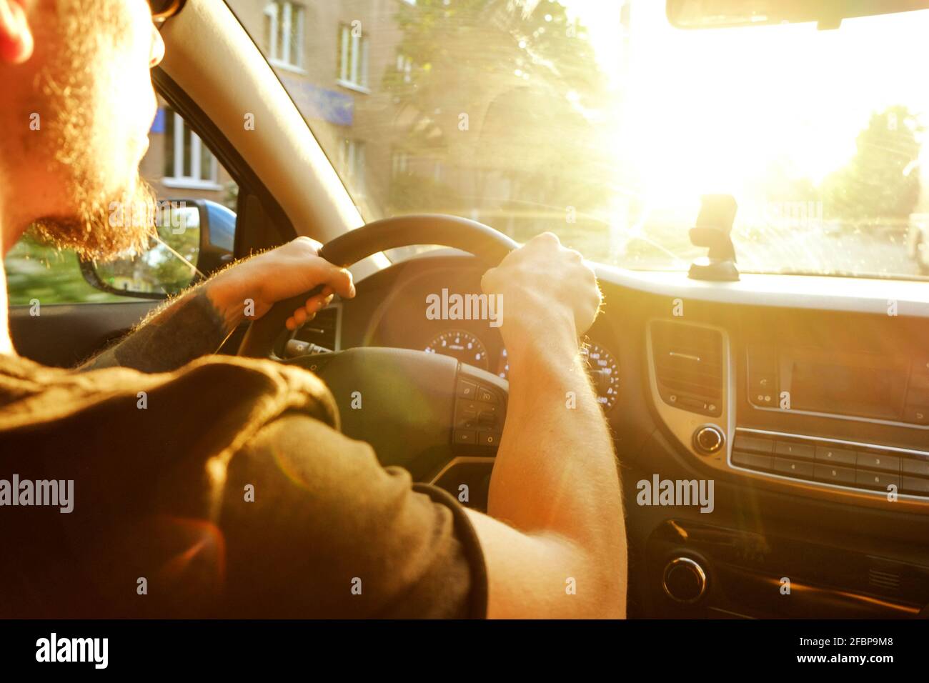 Jeune homme en t-shirt noir tenant le volant, voiture de conduite, tatouage avant-bras, mains gros plan. Panneau de tableau de bord, support de téléphone. Mâle intérieur vehic Banque D'Images