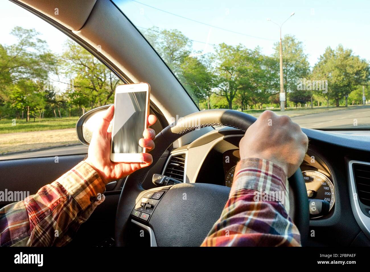 Gros plan sur les mains d'un jeune homme tenant le volant de la voiture. Panneau de tableau de bord, support de téléphone. Homme d'affaires conducteur, intérieur du véhicule, coucher de soleil Banque D'Images