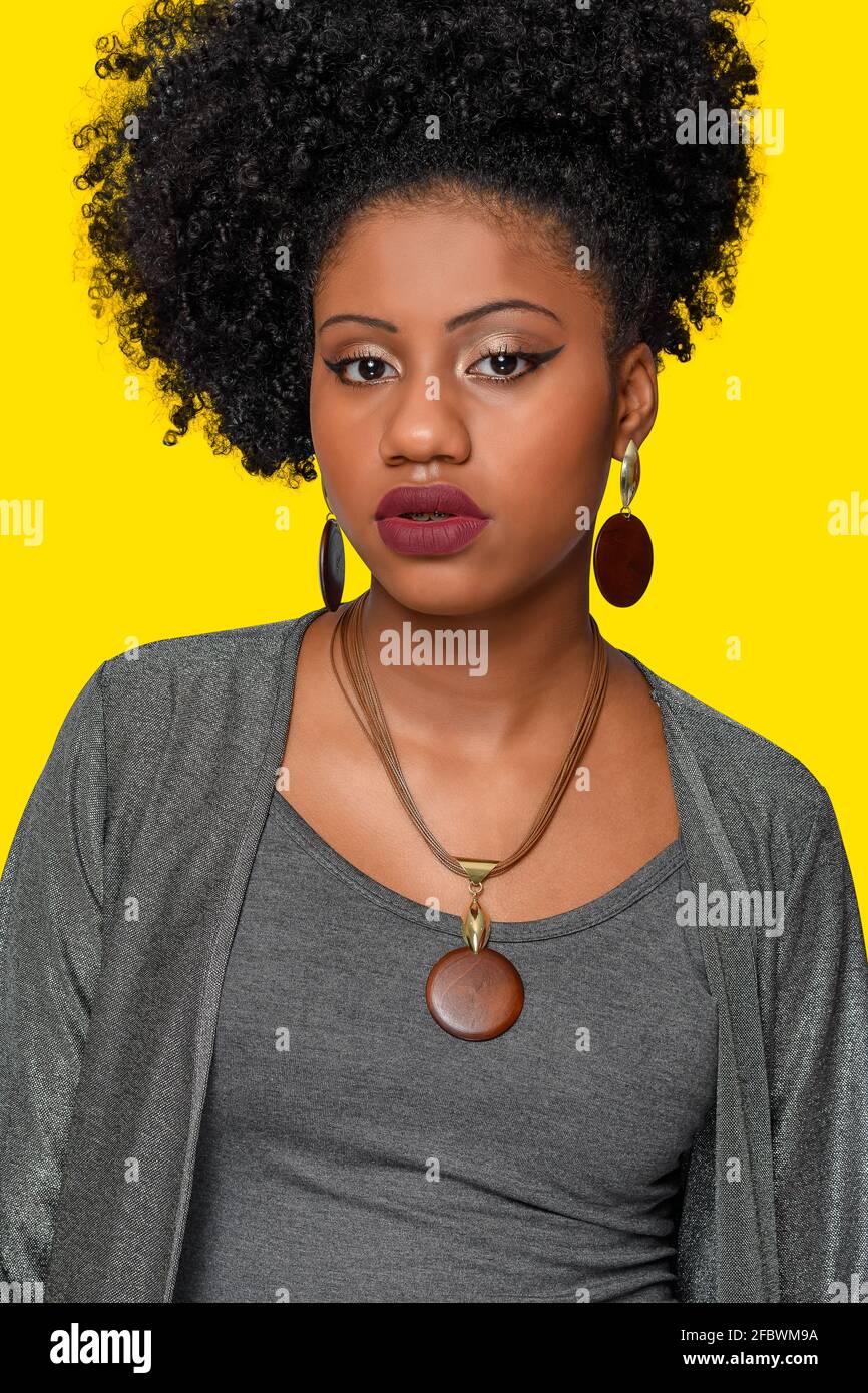 magnifique afro brésilien adolescent modèle portant un collier en bois et  des boucles d'oreilles avec des détails dorés, portant des vêtements gris  isolés sur fond jaune Photo Stock - Alamy