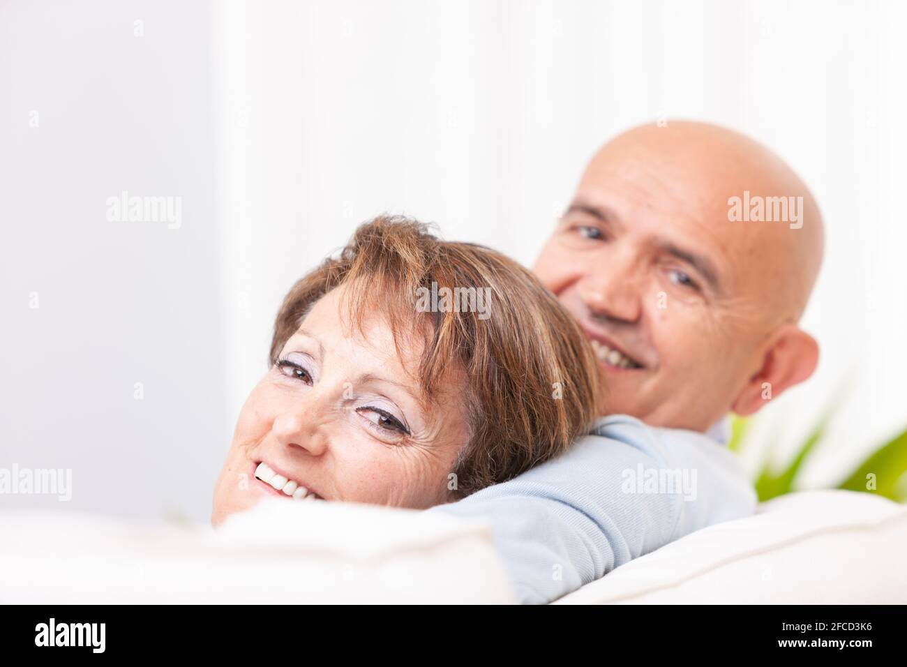 Un couple d'âge moyen sympa qui regarde de nouveau sur le dessus d'un canapé à l'appareil photo avec sourires heureux et mise au point la femme Banque D'Images