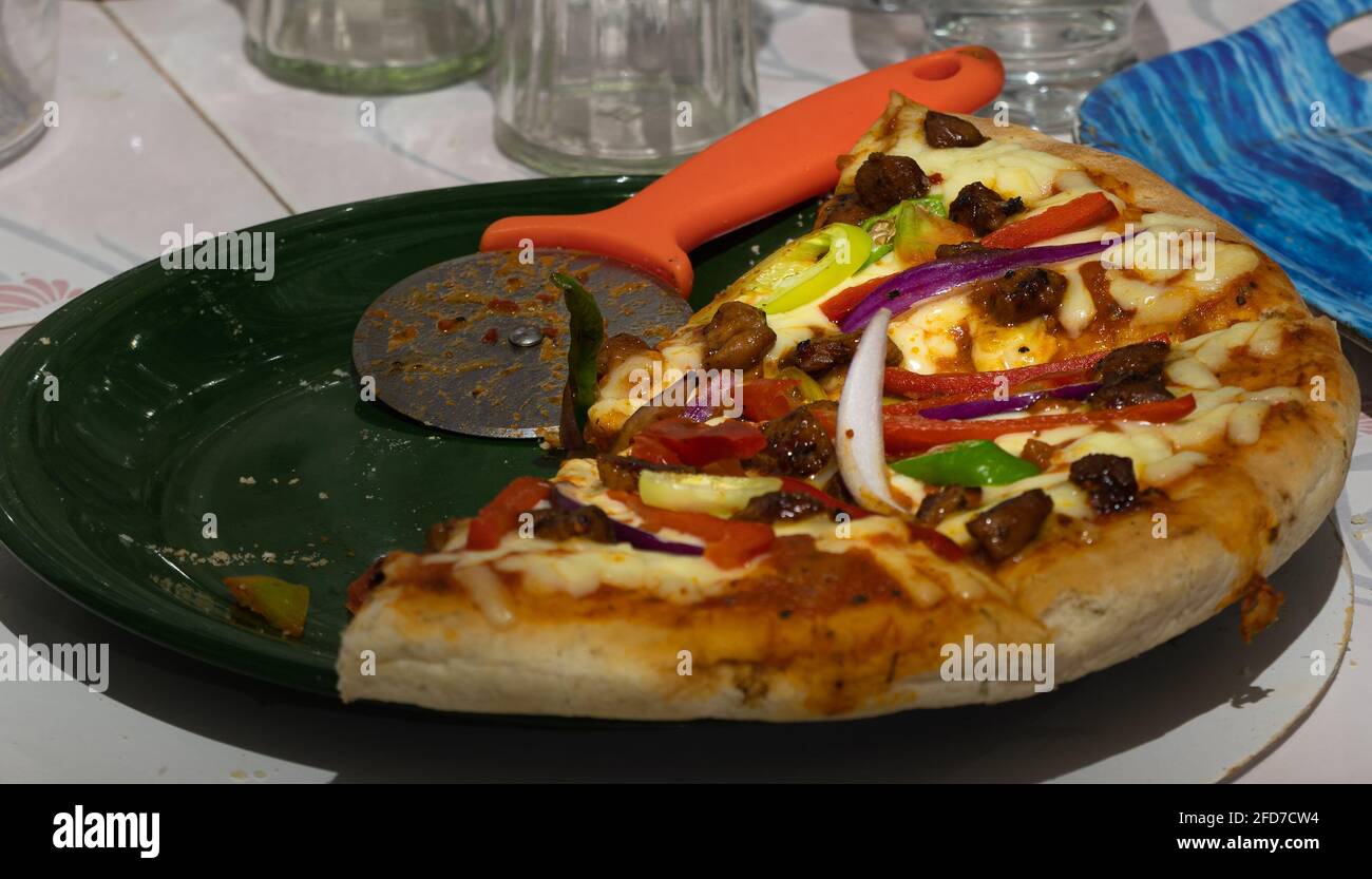 Pizza en tranches de restes à moitié mangées dans une assiette avec une roue de coupe de pizza dans la cuisine maison, garnitures de poulet au fromage avec oignons et poivron et épicé Banque D'Images