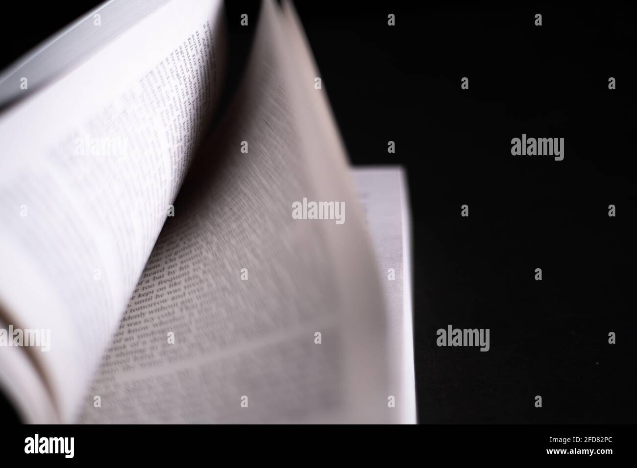 Défilement de pages dans un livre de roman anglais. Livre ouvert isolé dans un fond noir foncé. Concept de lecture fait un homme plein. Banque D'Images