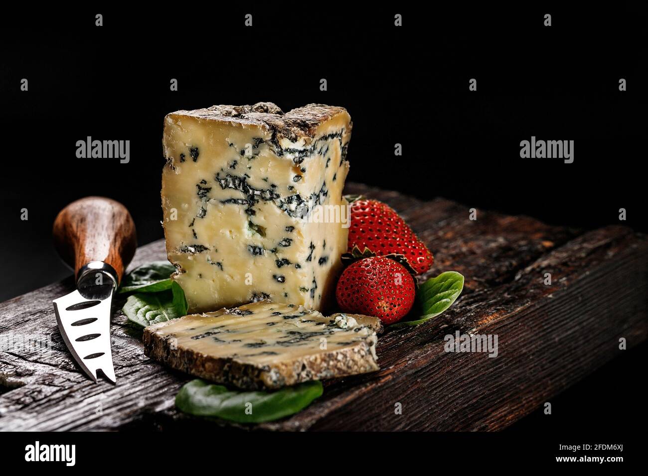 Fromage semi-doux avec moule à base de lait de vache. Le roi des fromages bleus est Stilton. Un morceau de fromage et des fraises mûres sur un panneau en bois sombre et Banque D'Images