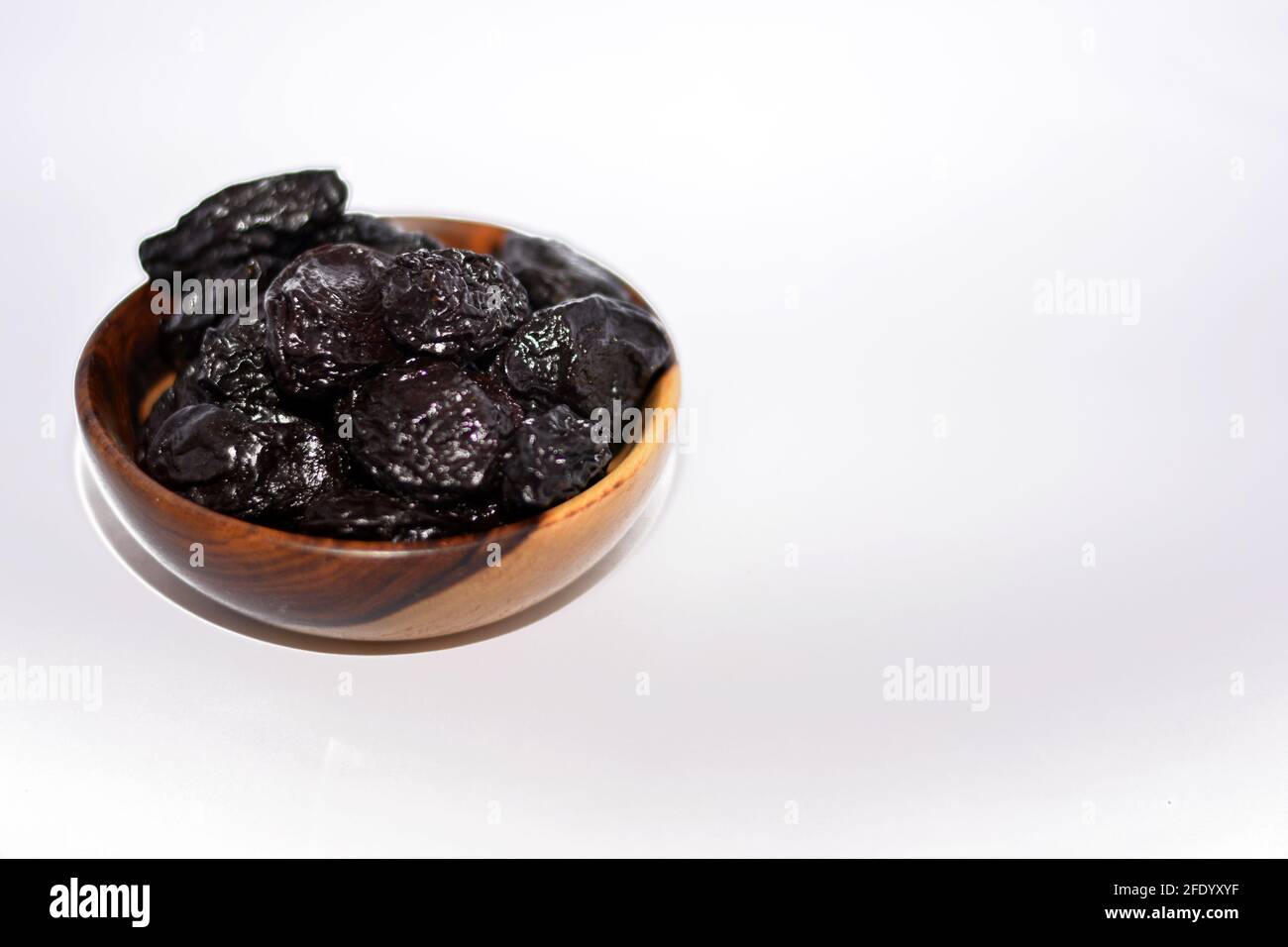 Pruneaux dans un bol en bois brun isolé sur fond blanc, collection de prunes séchées Banque D'Images