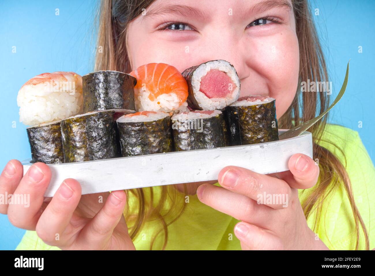 Une petite fille adorable aime manger des sushis. Joyeux drôle caucasien blonde petite fille avec divers rouleaux de sushi et baguettes. Sur fond bleu vif Banque D'Images