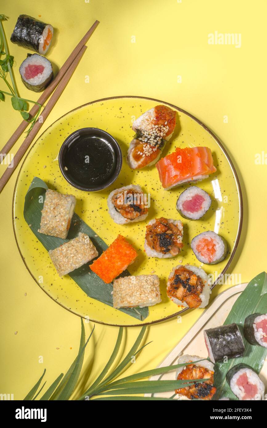 Petits pains à sushi avec riz et poisson, sauce soja et baguettes sur fond jaune, plat tendance à la lumière du jour Banque D'Images