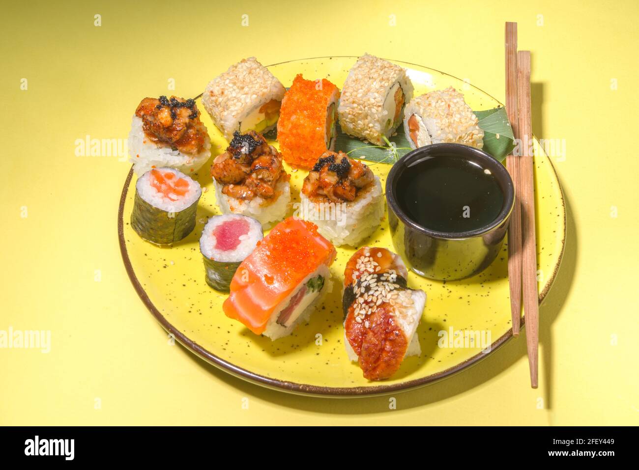 Petits pains à sushi avec riz et poisson, sauce soja et baguettes sur fond jaune, plat tendance à la lumière du jour Banque D'Images