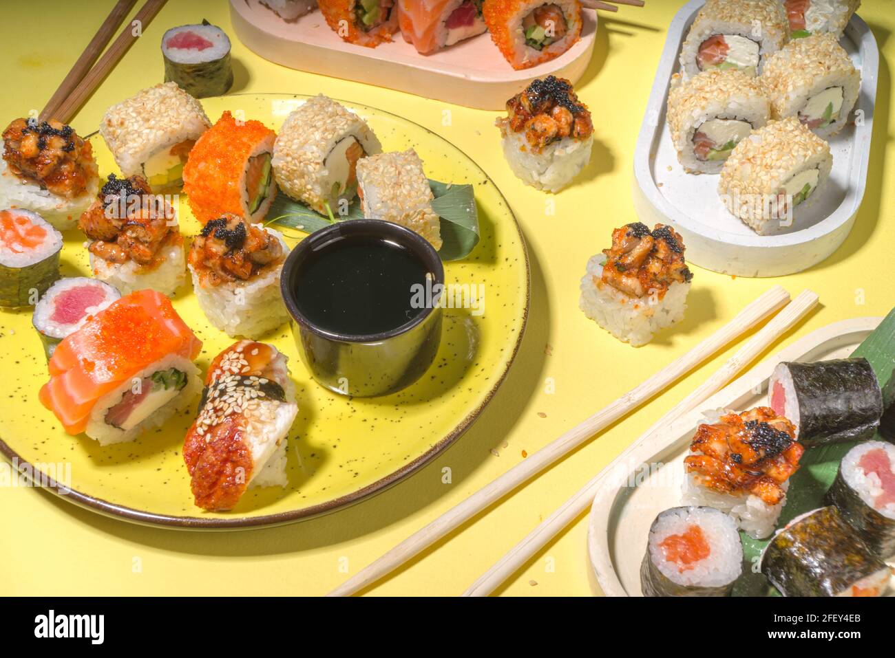 Petits pains à sushi avec riz et poisson, sauce soja et baguettes sur fond jaune, plat tendance à la lumière du jour Banque D'Images