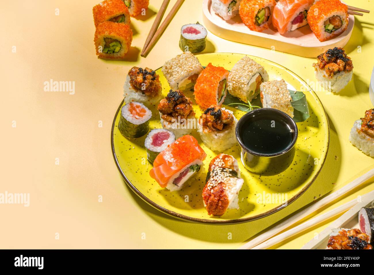 Petits pains à sushi avec riz et poisson, sauce soja et baguettes sur fond jaune, plat tendance à la lumière du jour Banque D'Images