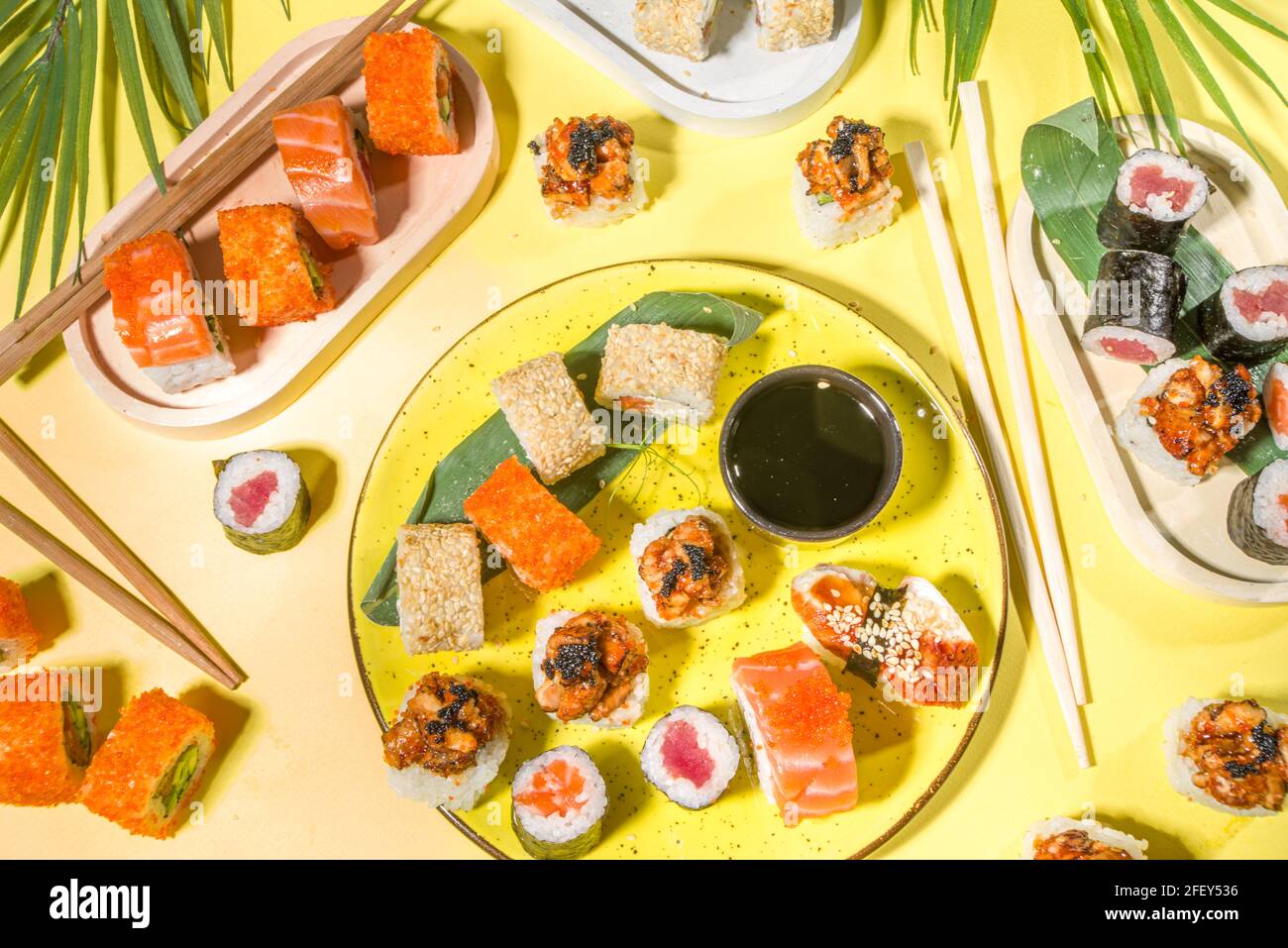 Petits pains à sushi avec riz et poisson, sauce soja et baguettes sur fond jaune, plat tendance à la lumière du jour Banque D'Images