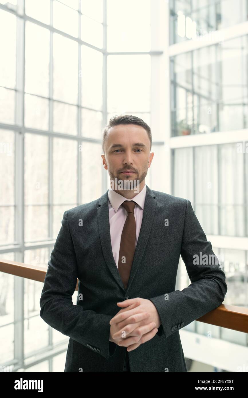 Portrait d'un homme d'affaires charmant et sérieux avec un chaume portant un costume classique et attachez la main courante dans le couloir du hall d'affaires Banque D'Images