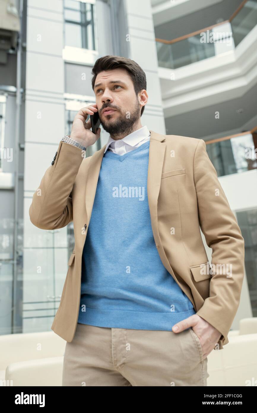 Un jeune avocat sérieux et confiant en costume beige se promenant dans le hall et appeler le client par téléphone Banque D'Images