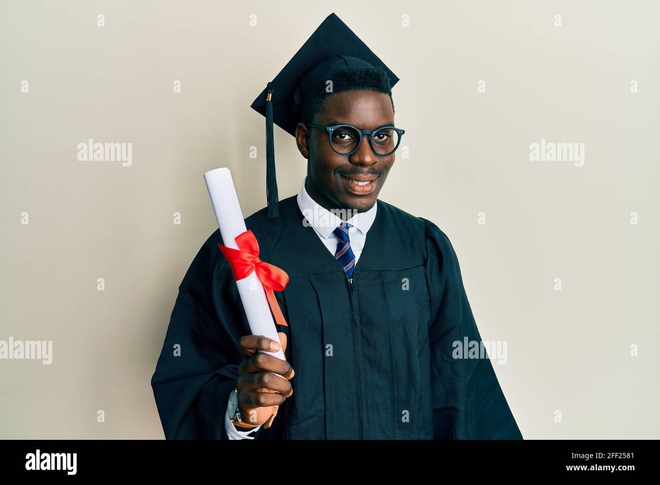 Beau homme noir portant une casquette de remise des diplômes et une robe de  cérémonie tenue diplôme ayant l'air positif et heureux debout et souriant  avec un sourire confiant, sho Photo Stock -