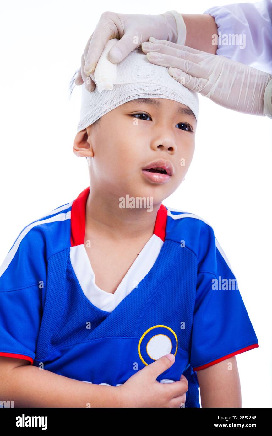 Blessures sportives. Athlète petit asiatique (thaïlandais) garçon en bleu sportswear avec traumatisme de la tête. Le médecin fait un bandage sur le patient de tête. Enfant malheureux, on W Banque D'Images