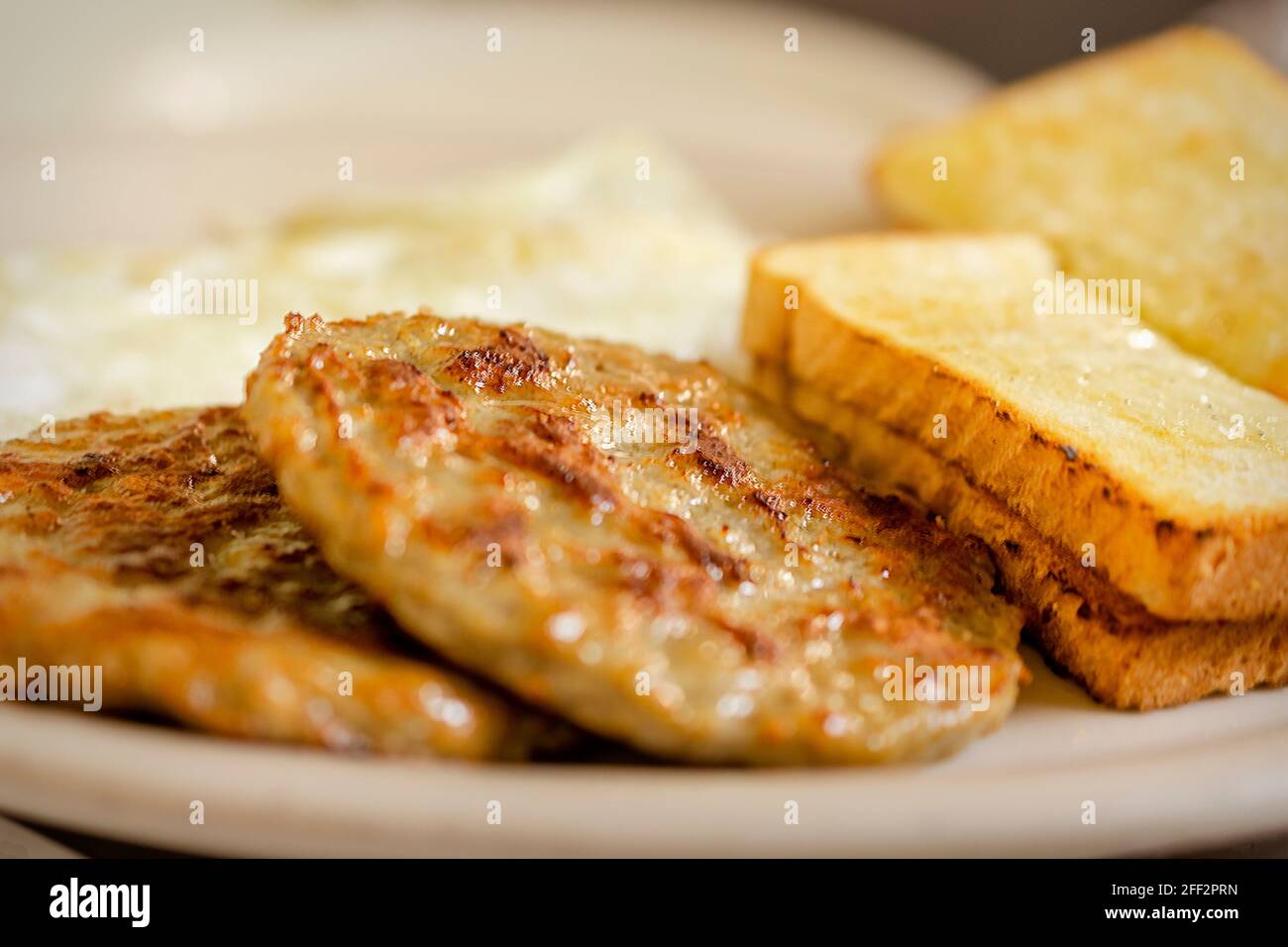 Un plat au petit-déjeuner comprenant 2 pâtés de saucisse de porc, deux piecesof de pain grillé blanc et 2 sur des œufs simples broutés en arrière-plan. Plaque blanche. Banque D'Images
