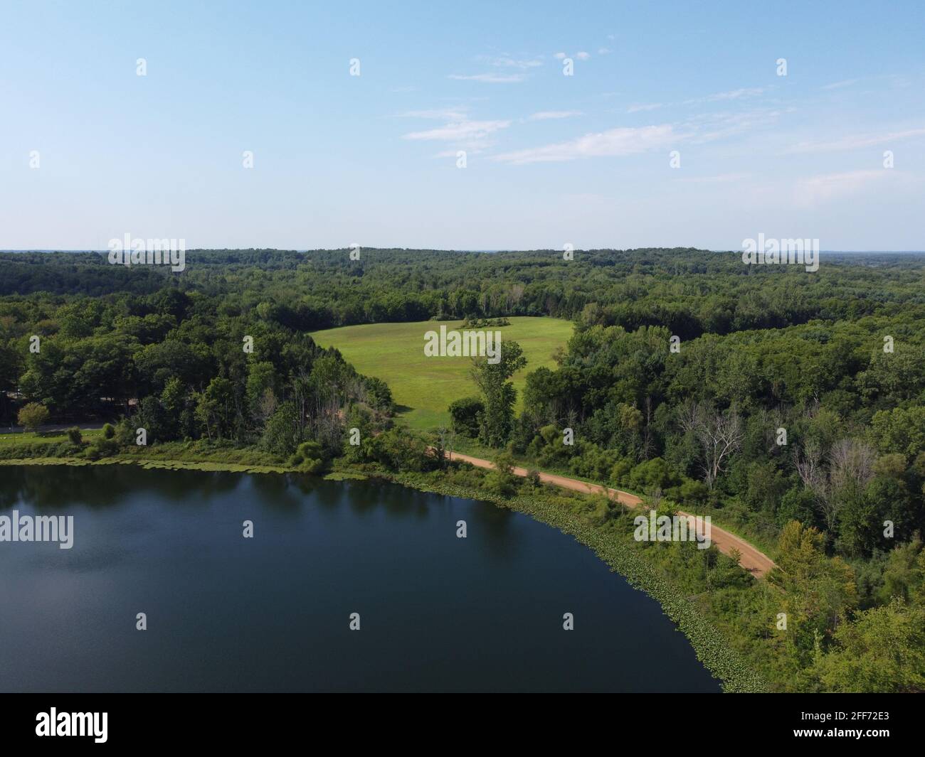 Photo aérienne d'une petite route arrière entourant un lac du Michigan qui sort d'une ligne d'arbres et de la ferme environnante. Banque D'Images