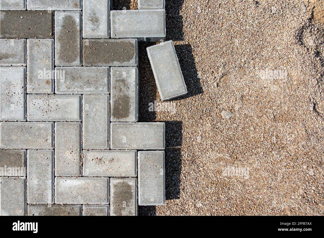 Pose de dalles de béton gris dans une passerelle. Processus de construction d'un trottoir pavé en briques, d'une route pavée à moitié construite Banque D'Images